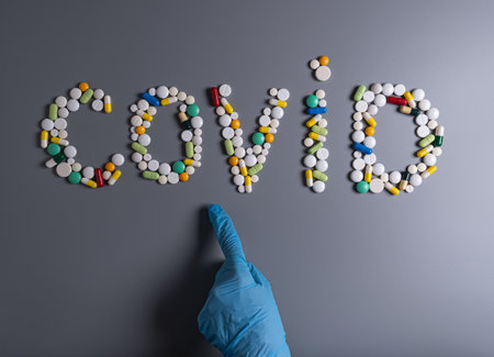 Hand in blue medical protective glove show sign COVID made of pills, tablets and capsules on gray table. Closeupの写真素材