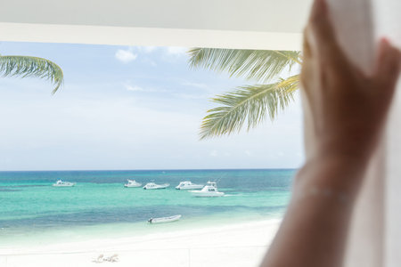 Woman open curtains in apartment, looking on sea view from balcony, selective focus on beach