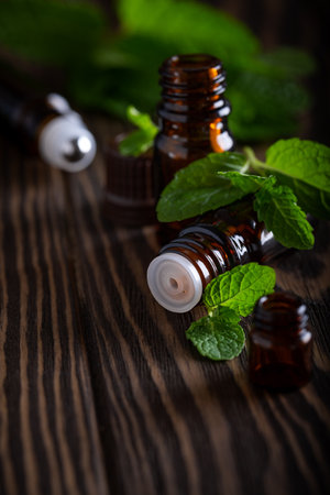 Set of amber bottles with essential oil decorated fresh mint leaves, herbal essence in dark glass jars on wooden board. Aromatherapy and alternative medicine conceptの写真素材