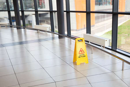 Cleaning service indoors. Yellow plastic caution sign - beware slippery on the floor at airport or shopping mall hall. Nobodyの写真素材