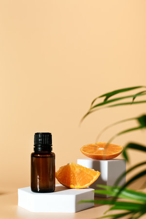Amber glass bottle with essential oil and citrus orange fruits on geometric podium on neutral color background, creative design with palm leavesの写真素材