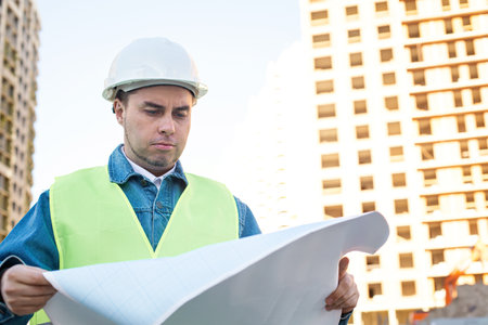 Engineer in white protective helmet looking at blueprint at construction site. Outdoorの写真素材