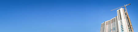 Building under construction. Crane move heavy tools on blue sky background. Long bannerの写真素材