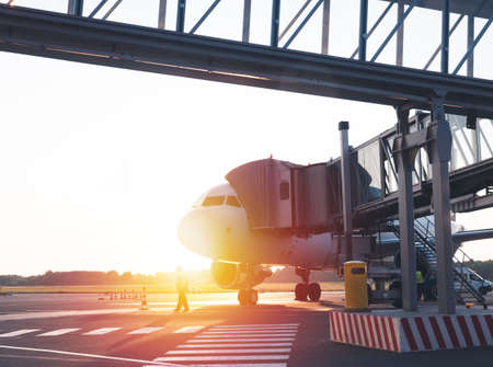 Airplane with terminal gangway of the airport building on sunset. Maintenance of aircraft before the flightの写真素材