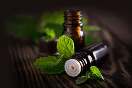 Set of amber bottles with essential oil decorated fresh mint leaves, herbal essence in dark glass jars on wooden board. Aromatherapy and alternative medicine conceptの写真素材