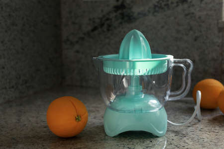 Electric juicer for making fresh citrus juice at early morning, mint color squeezer with orange fruits in kitchen interiorの写真素材