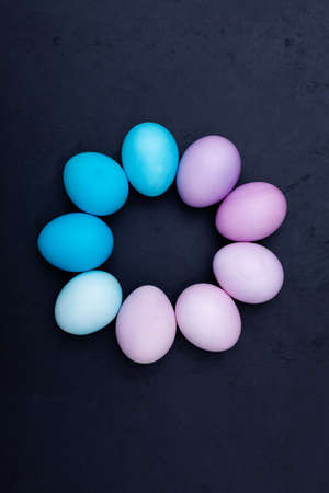 Happy easter trendy card lying in a circle shape blue and violet colored eggs on dark background, top viewの写真素材