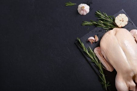 Raw and uncooked whole duck on slate board on black background. View above, frame with copy space