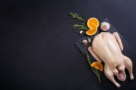 Raw organic, uncooked whole duck with cut orange and rosemary on slate board on black background. Frame with copy spaceの写真素材