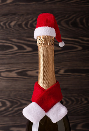 Champagne bottle wearing christmas hat and red knitting scarf on wooden background. new year celebrationの写真素材