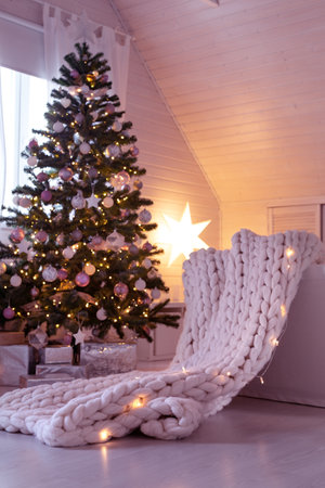Beautiful decorated evergreen shiny fir tree with white and pink color balls with garland lights. Christmas scandi decoration at home. New Year Hygge interior, no people.の写真素材