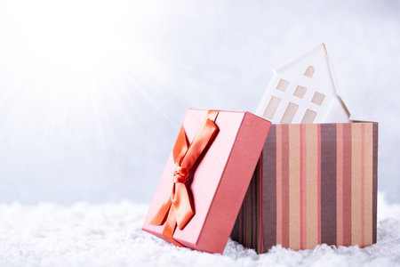 Small white house in red gift box on snow over silver background, closeupの写真素材