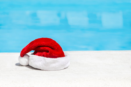 Santa Claus hat near swimming pool with clean turquoise water. Christmas and New Year celebration at poolsideの写真素材