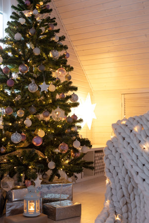 Beautiful decorated evergreen shiny fir tree with white and pink color balls with garland lights. Christmas scandi decoration at home. New Year Hygge interior, no people.の写真素材