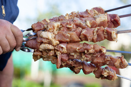 Man hand holds meat kebab with pork. Grilled barbecue shashlik on skews. close upの写真素材