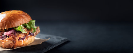 Pulled pork burger on dark background. Fastfood sandwich on craft paper and slate platter. takeaway food. Long banner for menuの写真素材