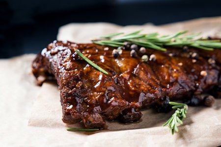Pork grilled ribs with rosemary and pepper on craft paper on dark background.の写真素材