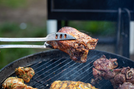 Cooking different meats on barbecue. Grilled and roasted lamb steaks on bbq. Take one piece with grill tongs. outdoorsの写真素材