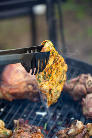 Cooking different meats on barbecue. Grilled and roasted lamb steaks on bbq. Take one piece with grill tongs. outdoorsの写真素材