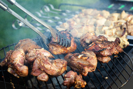 Cooking different meats on barbecue. Grilled and roasted lamb steaks on bbq. Take one piece with grill tongs. outdoorsの写真素材