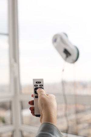 Woman washing and cleaning windows with smart vacuum cleaner. using remote controller. closeup on handの写真素材