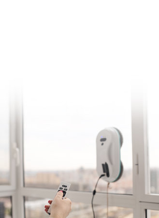 Woman washing and cleaning windows with smart vacuum cleaner. Using remote controller. Closeup on handの写真素材