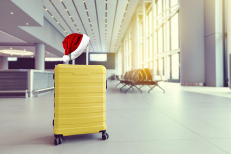Santa hat on yellow suitcase in airport terminal, travel concept. New year holidays. Christmas vacationの写真素材