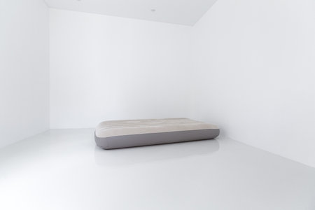 Portable air inflating mattress on white ceramic floor at empty room, concept on moving to new home or renting apartment without bedの写真素材