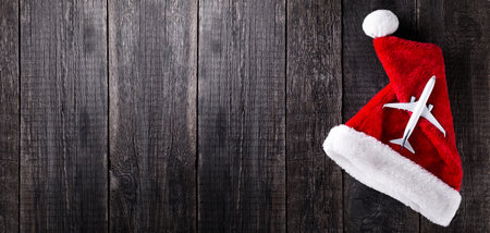 Airplane toy on Santa Claus hat on wooden rustic background. Christmas and new year celebration. Long bannerの写真素材