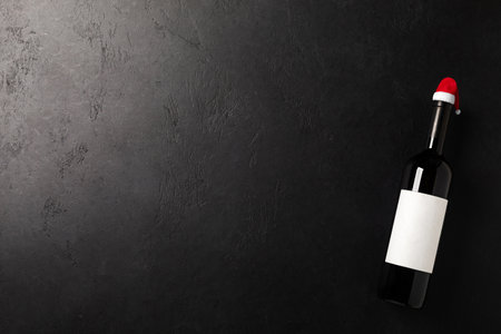 Santa claus hat on bottle with red wine and glass on black background. Flat lay. Christmas celebration. New year decorationの写真素材