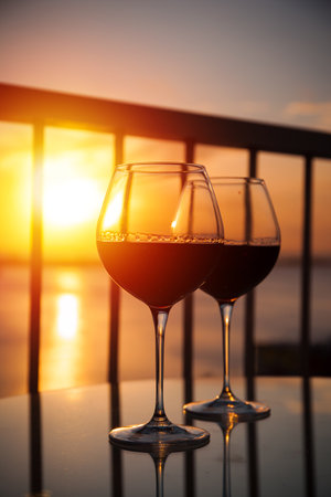 Two red wine glasses in front of the setting sun. Balcony view with Caribbean sea backgroundの写真素材