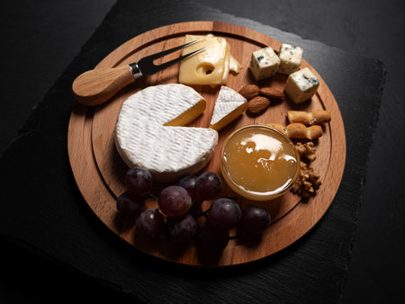 Sliced Brie cheese served with knife, honey, nuts and grape on wooden board. Closeupの写真素材