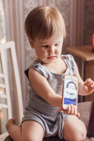 A small child sits on a table, playing with a smartphone. There's a kitchen in the background.のeditorial素材