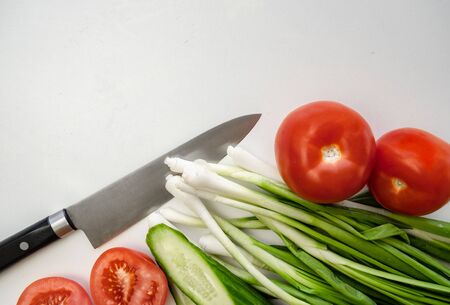 Fresh green onions, tomato and cucumber cut into slices with a knife on a white background. concept of vegetarianism, healthy eatingの写真素材