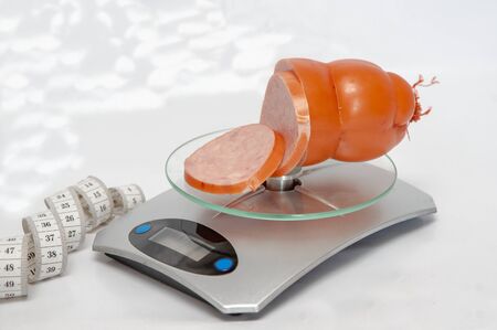 Measuring tape and slices of sausage in a digital kitchen scale on a white background.の写真素材