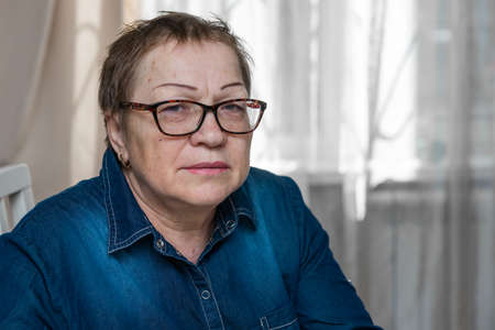 An elderly, old sad woman with glasses looks at the cameraの写真素材