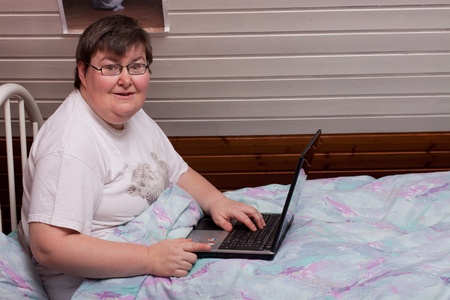 mentally disabled woman in her bed with laptop points to viewerの写真素材