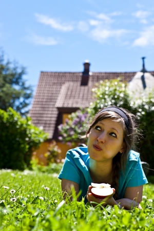 young woman is lying on grass and eats an appleの写真素材