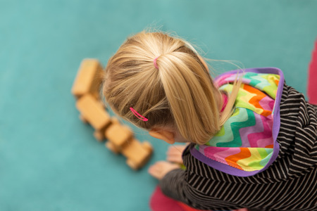 young blond girl is playing with a wooden toyの写真素材
