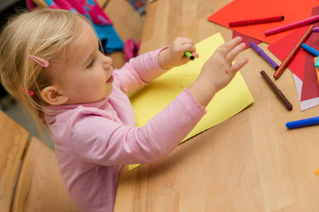 Blond cute girl is painting a picture with a lots of pencilsの写真素材