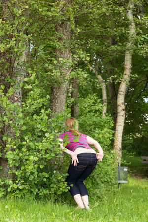 woman is peeing outdoors behind bushesの写真素材