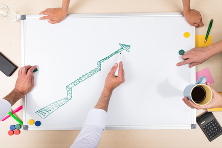 positive balance on whiteboard, overhead view with multiple handsの写真素材