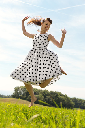Pin up Girl with white petticoat dress is jumping in the meadowの写真素材