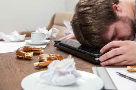 a man with burnout sleeping on his dirty deskの写真素材
