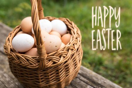 basket with white and brown bio eggs, green meadow in the background, text happy easterの写真素材