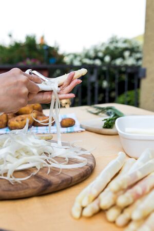 white and green asparagus on a table with new potatoes, woman is peeling the asparagus, close upの写真素材