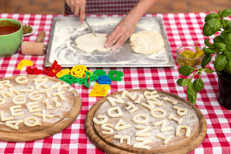 woman cuts out letters, dough on a griddle, red white tablecloth, wooden boards with lot of lettersの写真素材