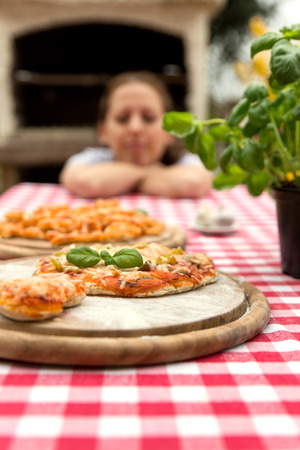 woman with baked pizza in front of a pizza stove, red white tableclothの写真素材