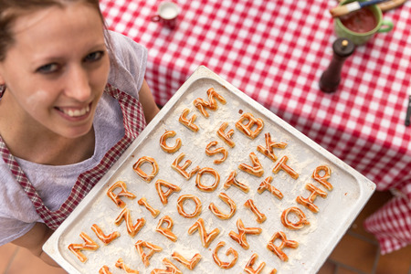 woman is holding a griddle, pizza dough with tomatoe sauce, lettersの写真素材