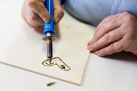 senior adult woman is doing woodburning as art therapy, horizontalの写真素材